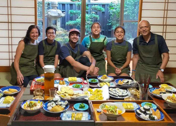 Guests at a Japanese home cooking class, smiling at the camera in front of a feast of traditional Japanese food.